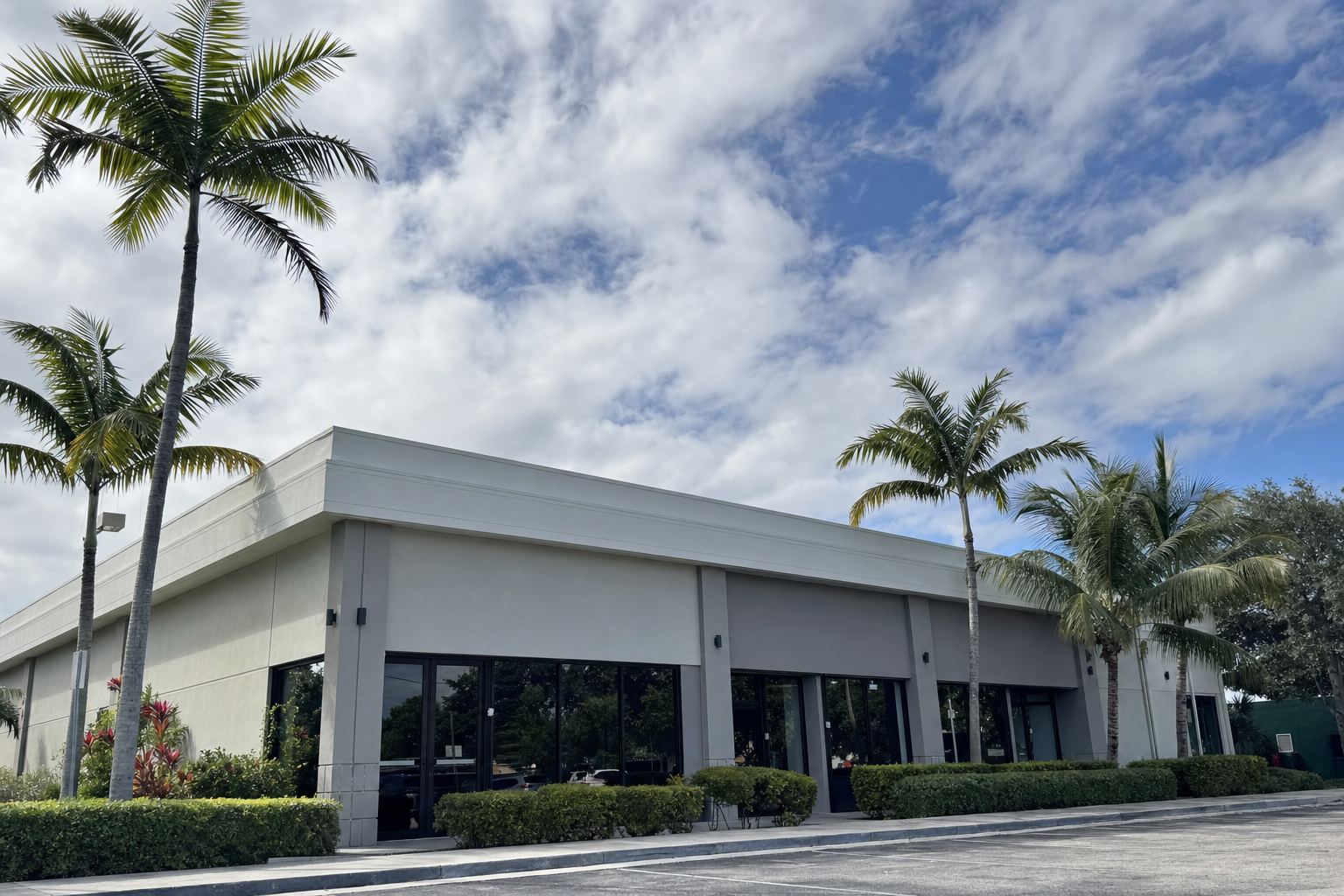 fotografía documental desde el suelo de un edificio comercial bajo en Miami con techo plano, cielo parcialmente nublado, palmeras, fachada limpia, sin texto ni logotipos