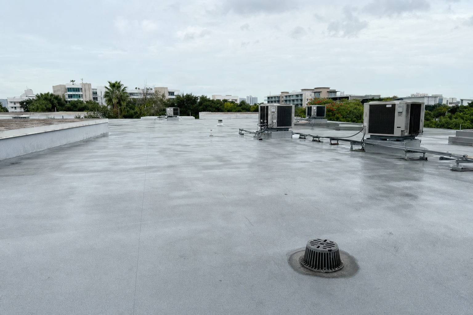 foto documental de un techo comercial plano en Miami después de lluvia ligera, superficie casi seca con drenaje despejado funcionando correctamente, cielo nublado claro, edificios bajos al fondo, sin personas ni texto