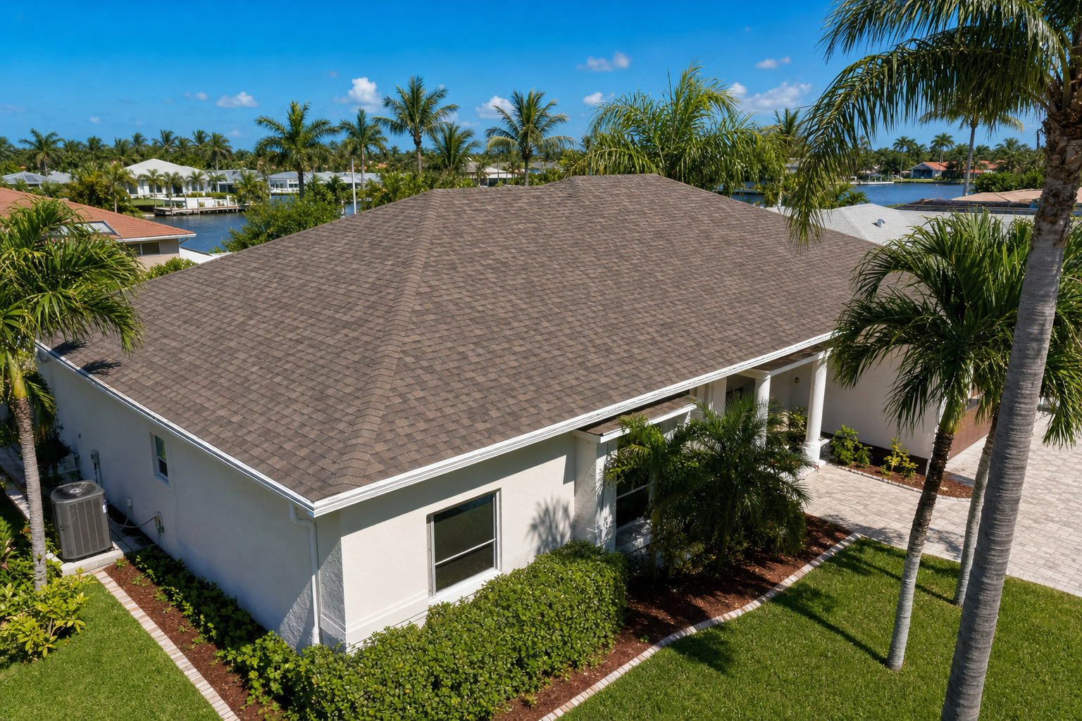 45-degree drone photo of a South Florida shingle roof with visible ridge line, soffit overhangs, palms, bright blue sky, realistic residential setting, no text