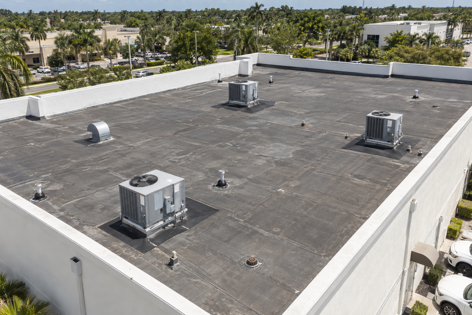 fotografía documental aérea a 45 grados de un techo comercial plano en el sur de Florida con superficie asfáltica multicapa, parapetos blancos, drenajes visibles, cielo soleado, sin texto ni logotipos